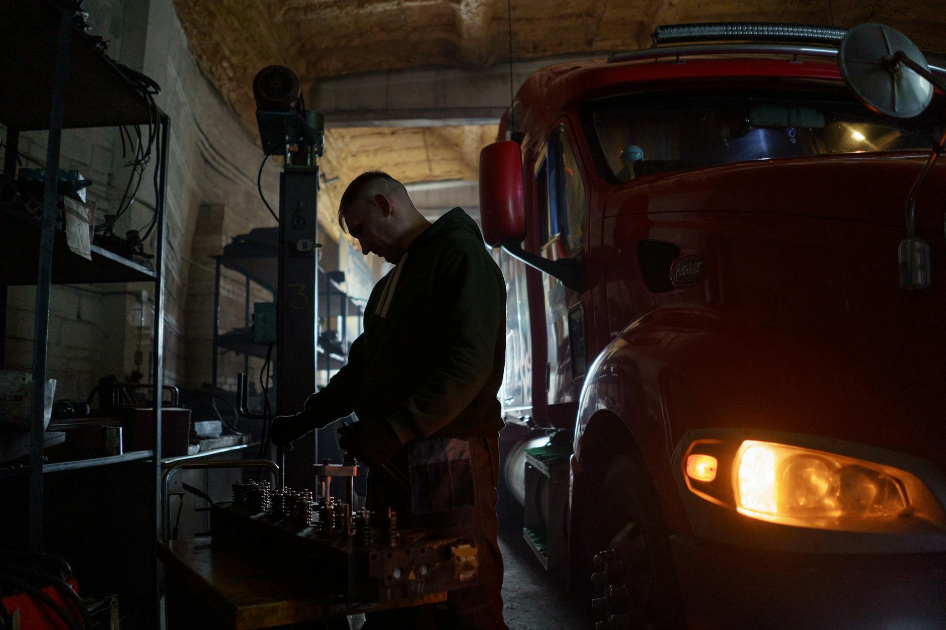 Mechanik pracuje przy dużej czerwonej ciężarówce w warsztacie Mechanik pracuje przy dużej czerwonej ciężarówce w warsztacie